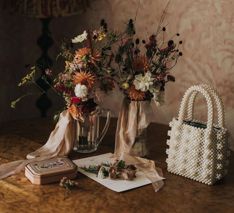 Pearl wedding bag with glass vases full of rustic locally sourced or homegrown wedding flowers 