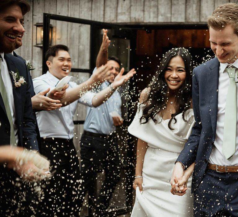 Bride in elegant off the shoulder gown walking with the groom for their confetti moment after their ceremony 