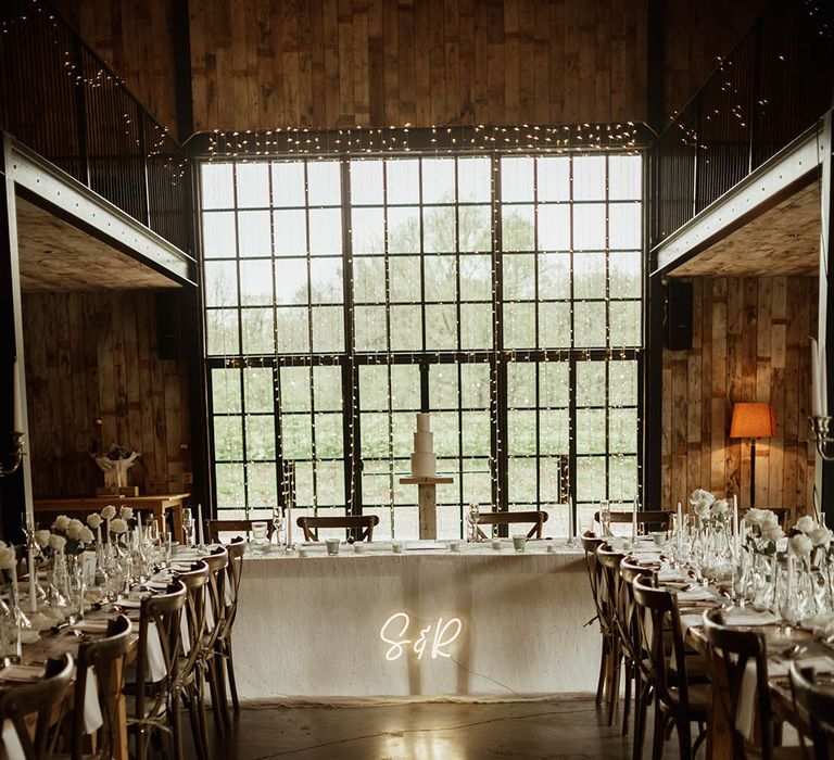 U-shaped wedding tabes decorated with fairy lights and candles with a custom neon sign and classic white wedding cake with pearls 