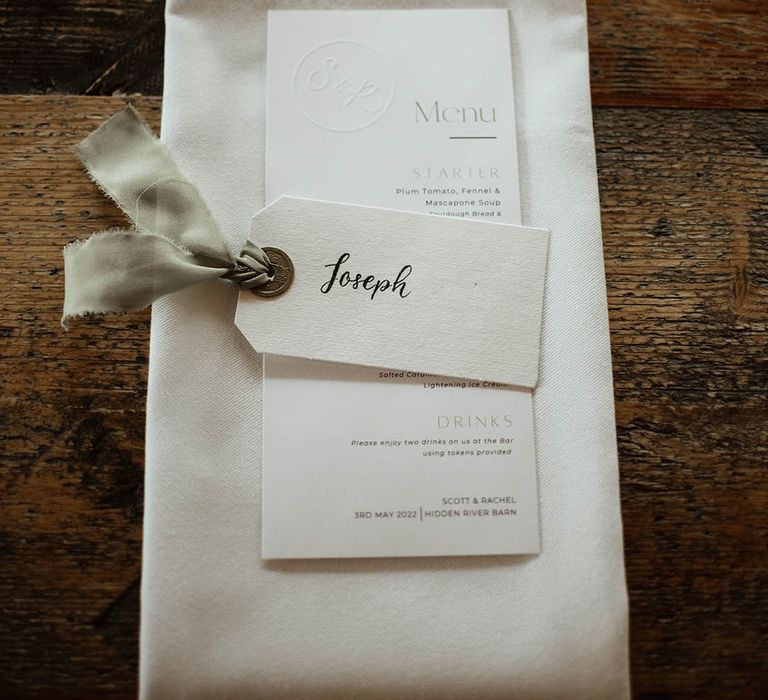 Simple white napkin and white menu with a vintage looking name tag for place name with sage ribbon detail 