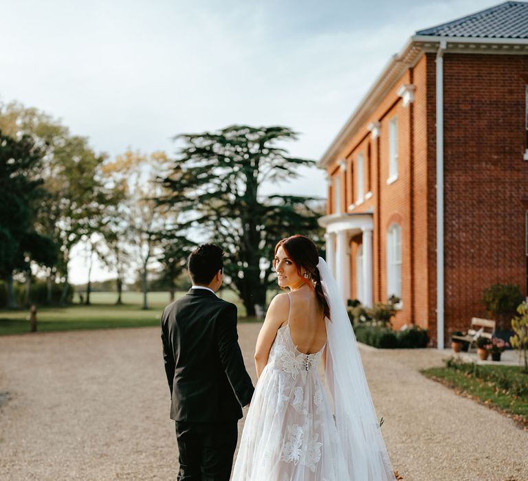 Bride looks back toward the camera in Madi Lane Bridal wedding dress with sheer floral design and cathedral veil 