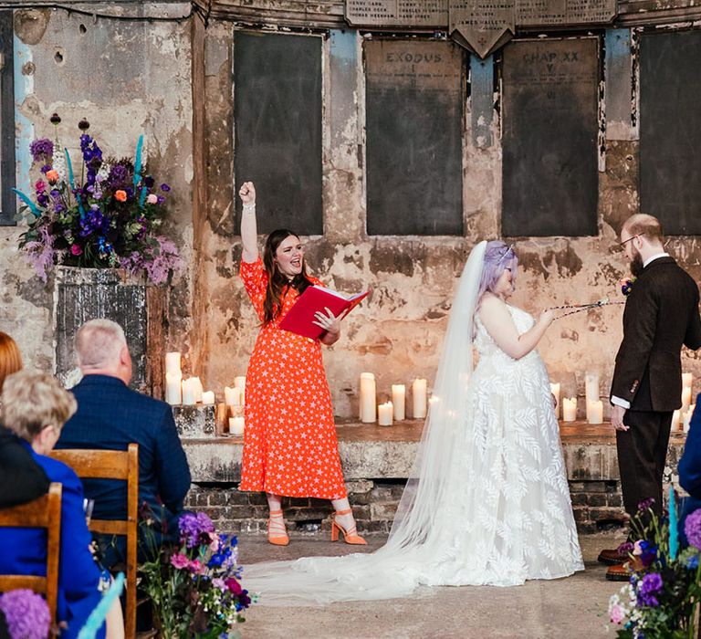 Groom in mocha brown textured suit and bride in leaf appliqué sheer Evie Young bridal gown and cathedral length veil at the alter of Asylum Chapel London wedding venue with celebrant doing bespoke wedding ceremony 