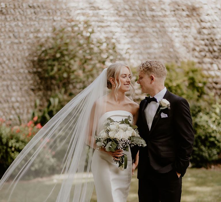 Bride in a strapless satin mermaid wedding dress smiling with the groom in black tie for Cissbury Barns wedding 