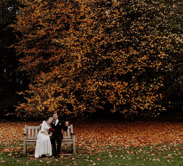 Autumnal wedding with the bride and groom sitting on a wooden bench together for their Halloween wedding 