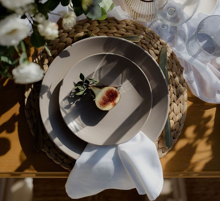 Wedding table place setting with fig, green and white floral decor, glasses and white tablecloth at private villa wedding in Greece