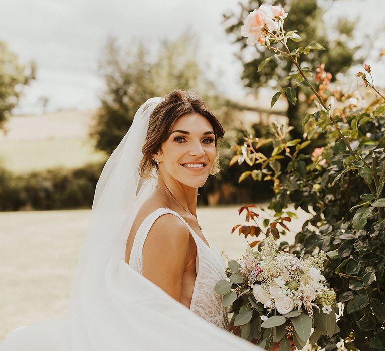 Bride in a fitted wedding dress wearing incredible wedding veil blowing in the wind 