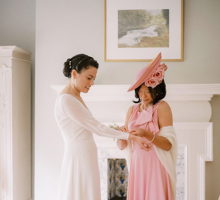 Mother of the bride in full pink wedding outfit helping the bride get ready for the wedding day 