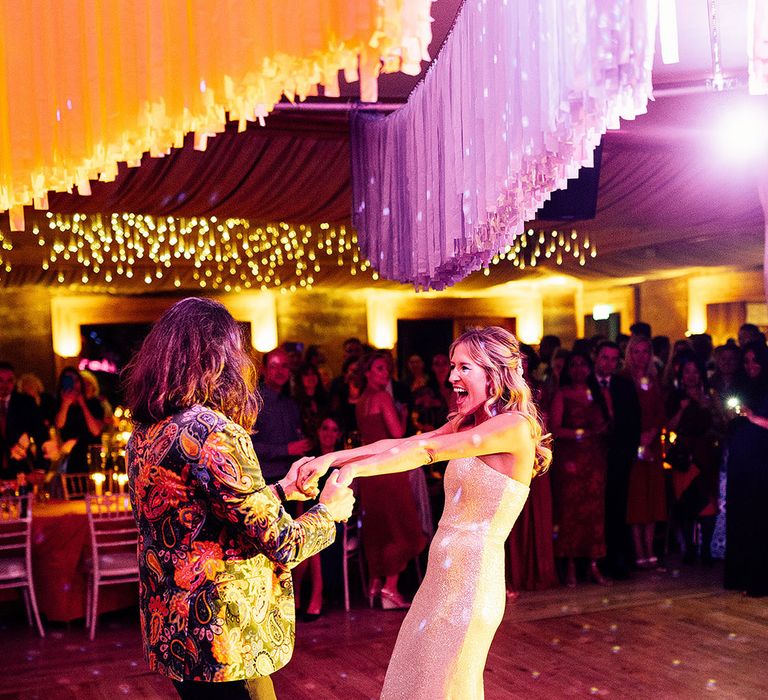 Bride in white sequin wedding reception dress with groom in neon patterned jacket for wedding first dance 