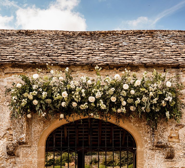 white and green wedding flower arrangement over a doorway at Caswell house Cotswolds wedding venue 