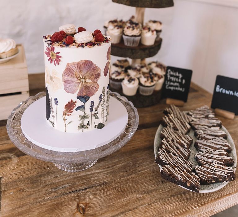 Pressed wildflower white iced wedding cake for intimate wedding with 55 guests on dessert table full of doughnuts and brownies 