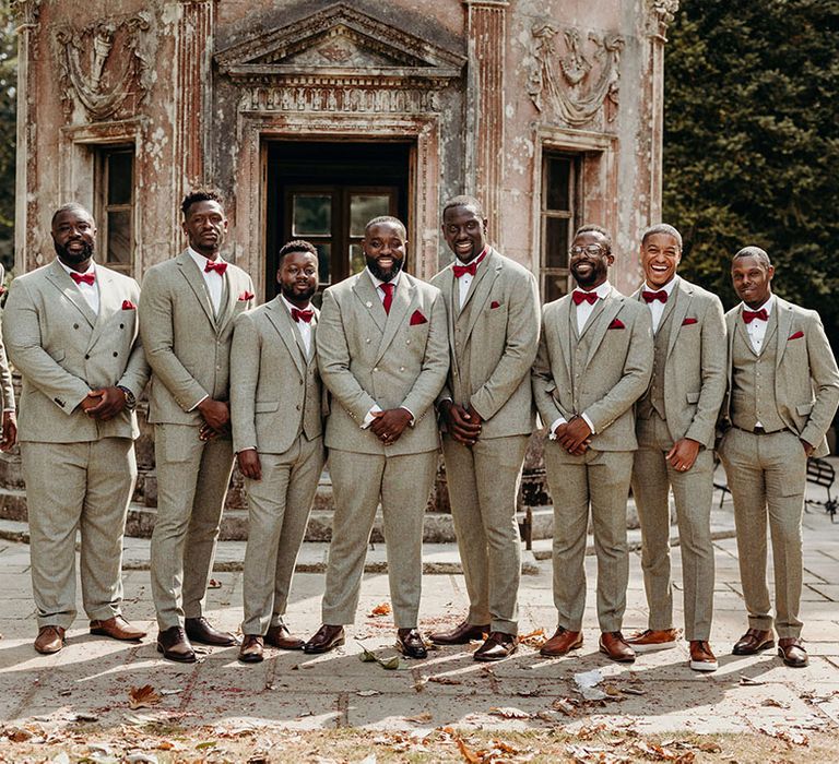 Groomsmen lined up in matching light grey double breasted suit jackets and bright red ties 