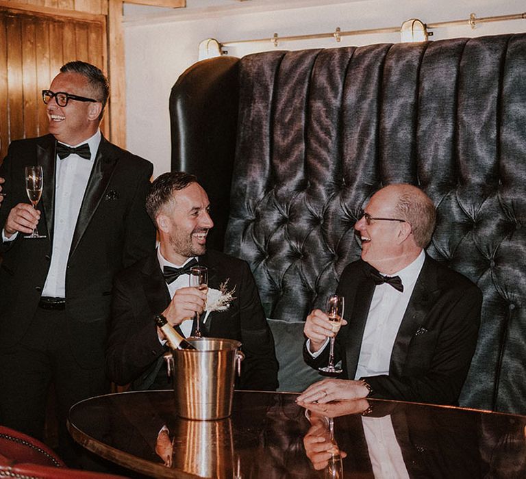 Groomsmen and groom in traditional black tuxedos laughing together 