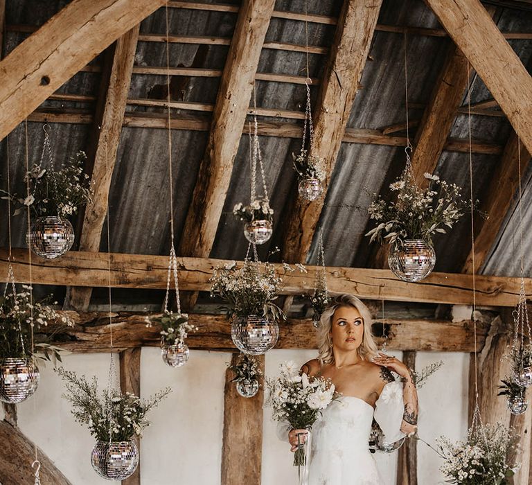 Bride in sweetheart off the shoulder wedding dress standing next to hanging disco plant pots and drinks trolley 