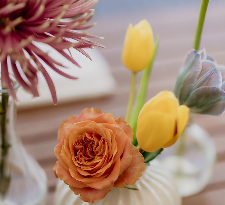 Orange rose and yellow tulip in a short ribbed white vase for table decor at destination wedding