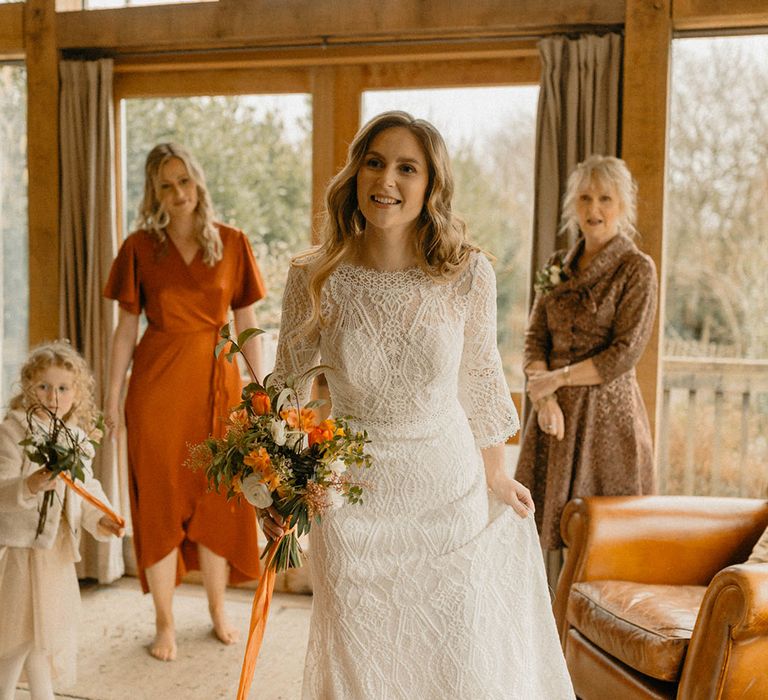 Barn wedding with bridal party in orange satin bridesmaid dresses and bride in lace long sleeve wedding dress 