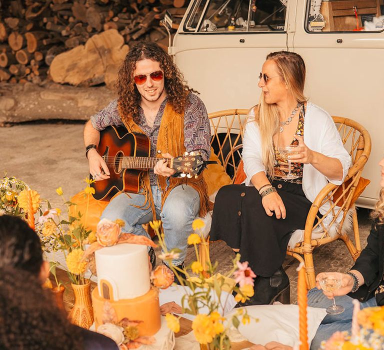 Wedding guests and musicians sit around the floor together at 60s and 70s inspired wedding 