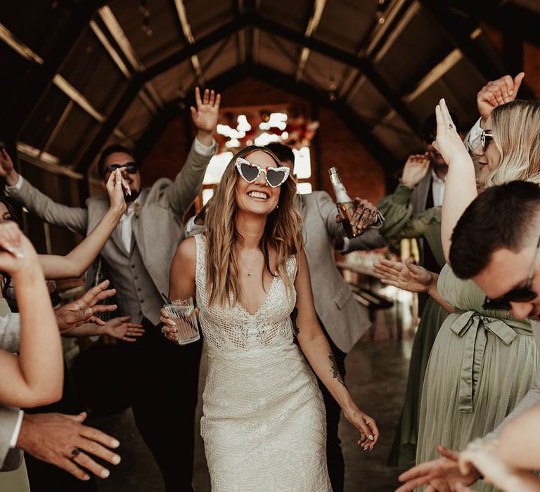 Bride in boho lace wedding dress with custom retro sunglasses surrounded by the wedding party 