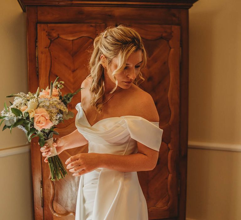 Bride wearing an off the shoulder wedding dress holding a pink rose wedding bouquet 