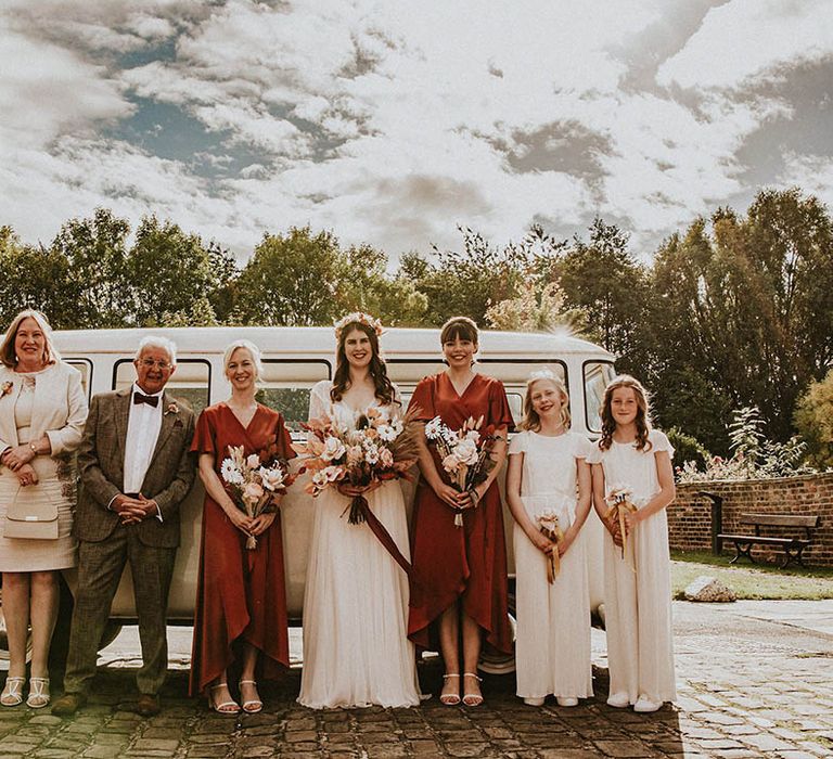 Bridal party with the bridesmaids in burnt orange satin bridesmaid dresses with the mother and father of the bride and flower girls in jumpsuits