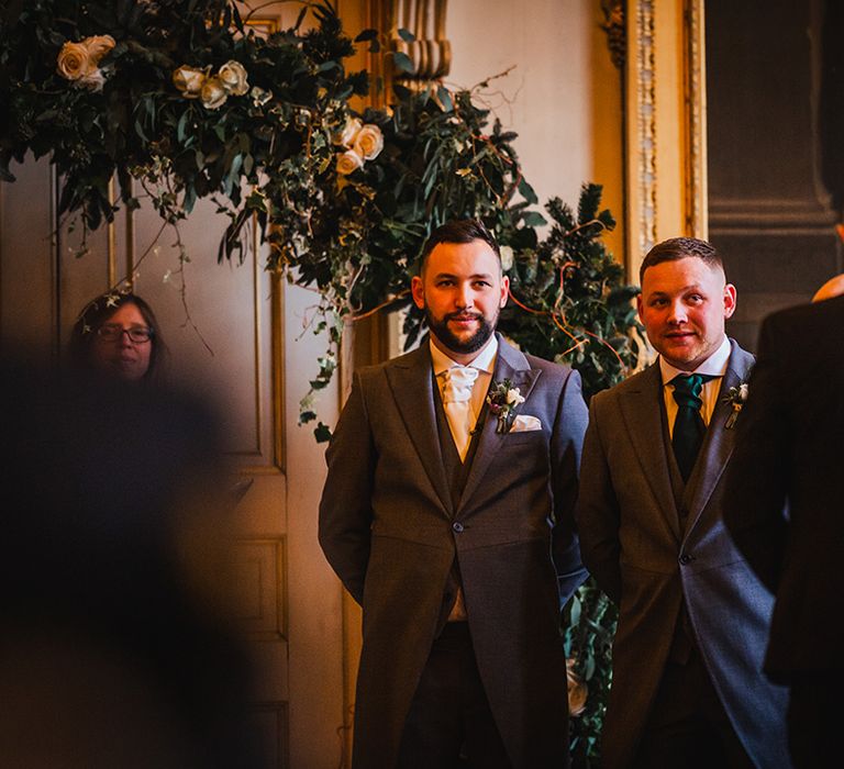 The groom and the best man stand side y side at the altar waiting for the bride 