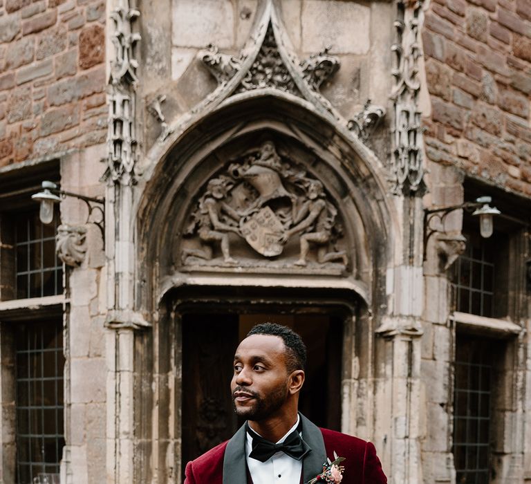 The groom in a red velvet suit jacket with a pink rose buttonhole 