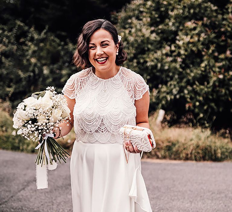 Bride holding a clutch bag in one hand and bouquet in the other hand by Carrie Lavers Photography