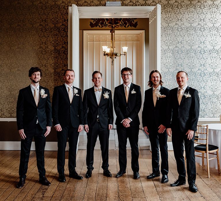 The groom and groomsmen wearing matching black suit jackets and champagne bow ties 