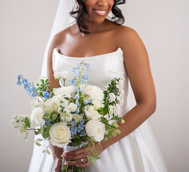 Bride holding white and blue wedding bouquet with white roses and foliage 