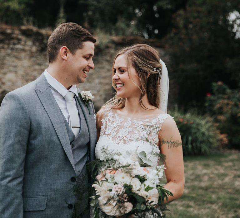 Groom in grey suit and bride in fitted wedding dress with lace illusion bodice 