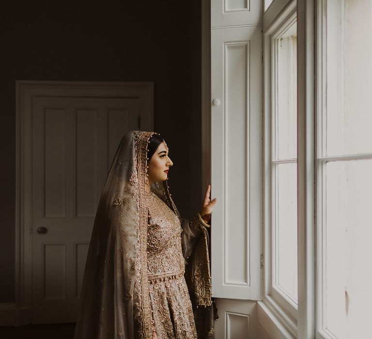 Muslim bride in a gold sari looking out of the window on her wedding day 