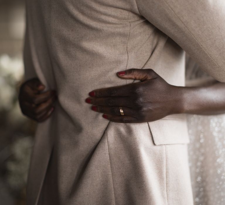 Bride embracing her groom in a beige suit with red manicure and gold wedding band 