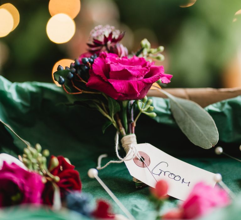 Pink floral buttonhole tied with string and a note that says 'groom'