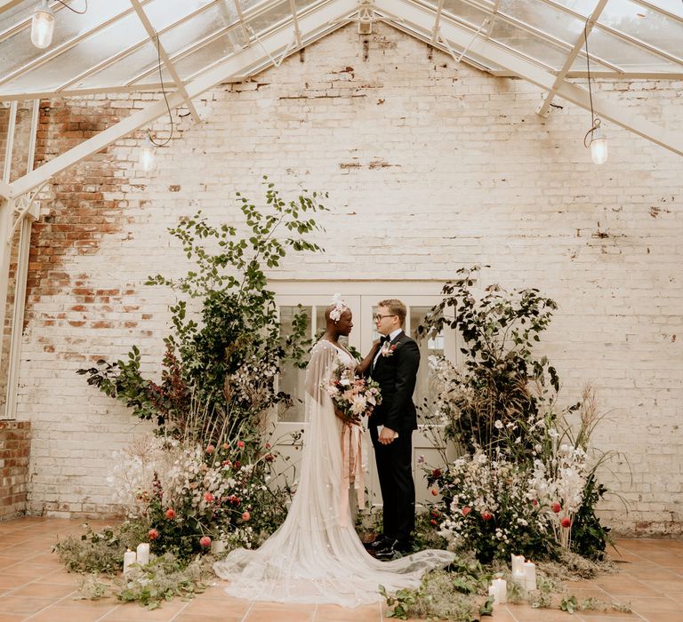 Intimate elopement wedding ceremony at Our Beautiful Glasshouse in Sussex with wildflower arrangements and bride and groom exchanging vows 