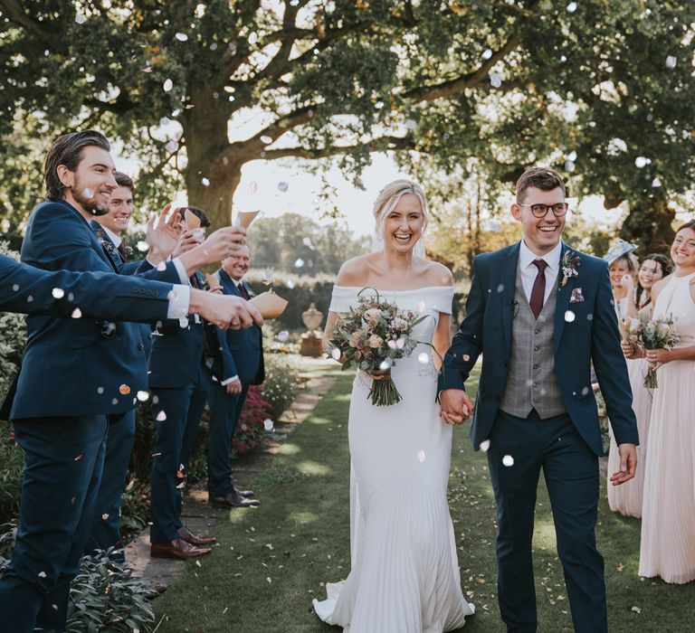 Bride & groom walk through friends and family with confetti being thrown around them