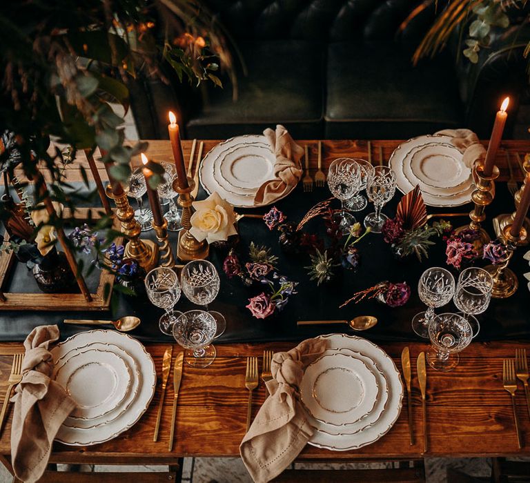 Opulent table setting with moody dark wedding flowers black table runner and gold candlesticks 