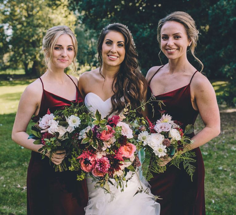 Bride with bridesmaids wearing deep red velvet bridesmaid dresses with pink rose bridal bouquets 