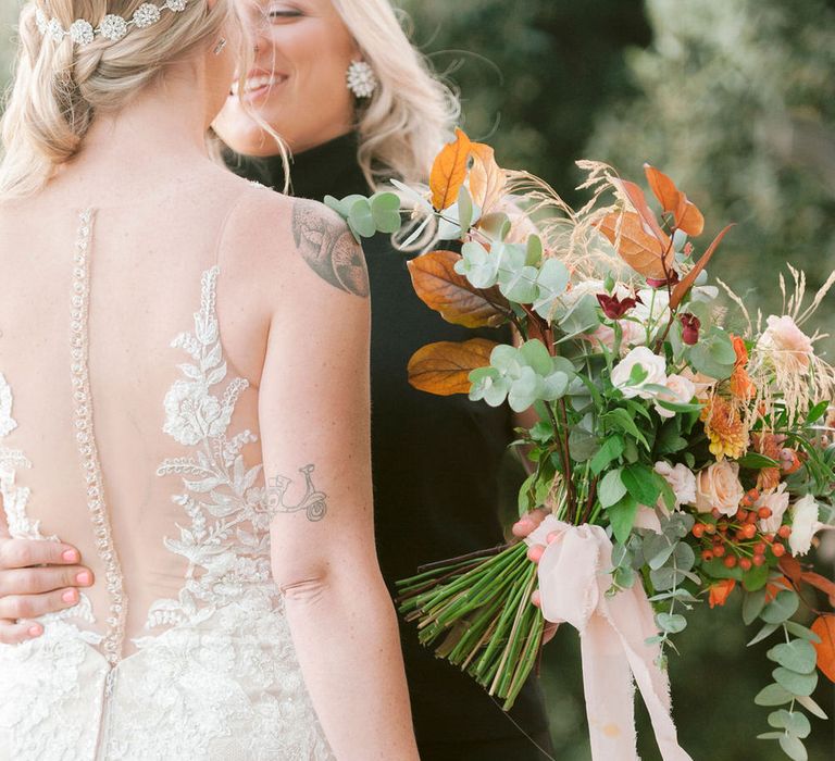 The brides hugging and holding their autumnal bouquets with roses, eucalyptus leaves and wild grass