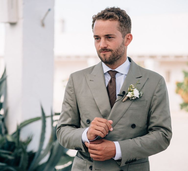 The groom fastening his cufflinks, wearing a grey Thom Sweeney suit