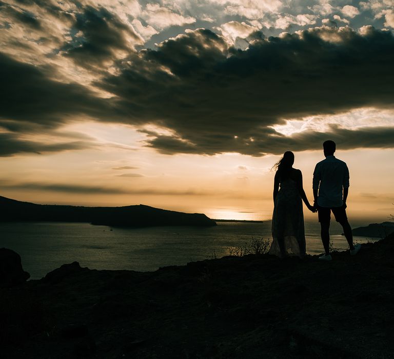 Outline of bride & groom holding hands as the sun sets behind them