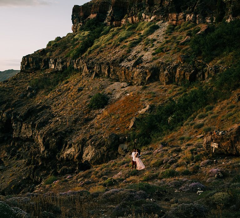 Bride & groom stand on rocks as they look out on to the ocean