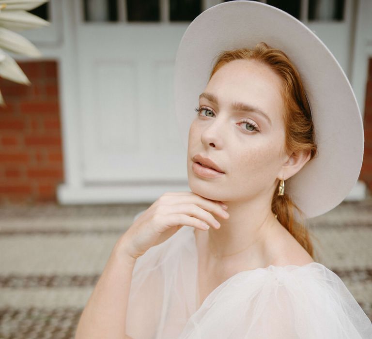 Bride wearing a blush pink stetson hat, puffed tulle shoulder wedding dress with plunge neckline and natural makeup, holding a bouquet of peonies