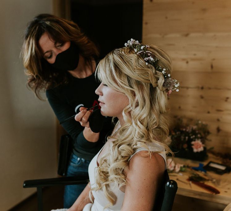 Bride with a half up half down wavy hairstyle wearing a delicate flower crown having her bridal makeup done