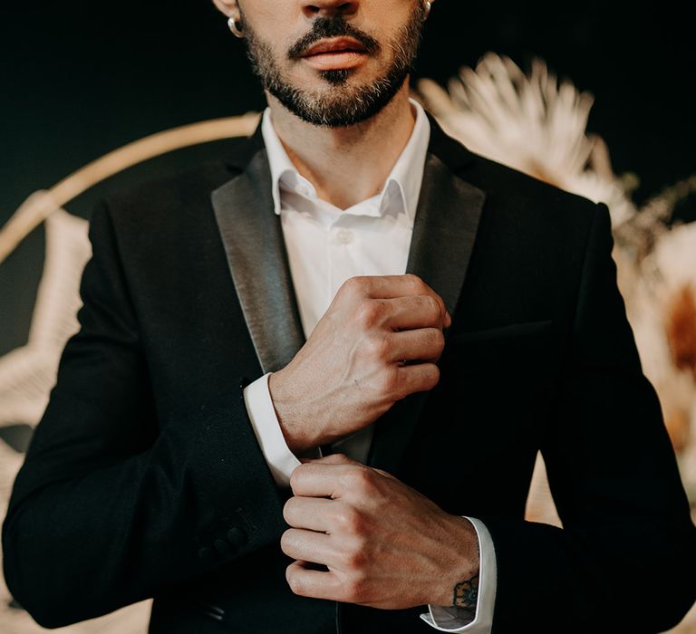 Groom does up cufflinks whilst wearing black tailored suit