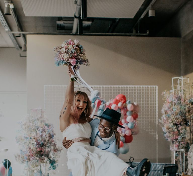 Groom in blue suit picking up his bride walking down the aisle of at their pastel wedding 