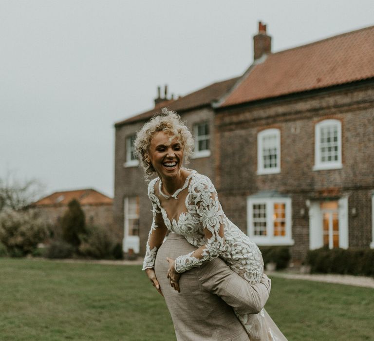 Curly haired bride wearing long sleeve embroidered wedding dress, being carried through a Hornington Manor