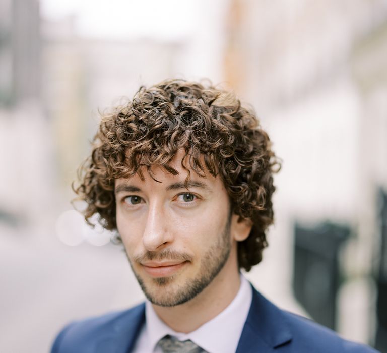 Groom looks toward camera whilst wearing blue suit and grey tie 