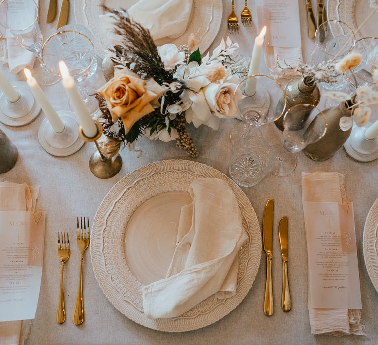 Place setting with ornate tableware, linen napkin and flower stems in cases 