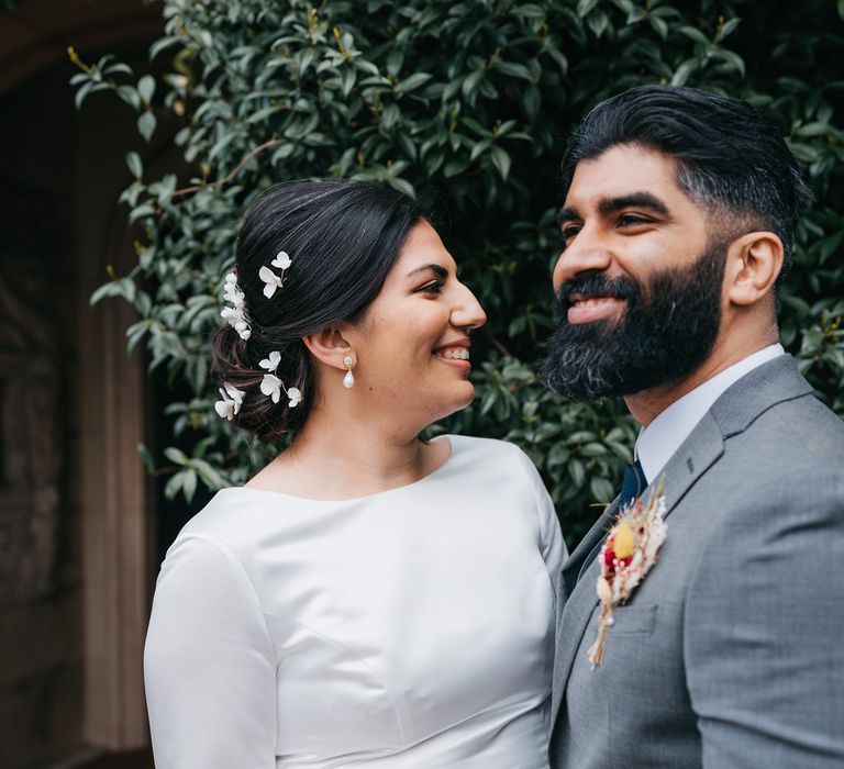 Bride & groom smile with one another on their wedding day whilst posing for photos outdoors