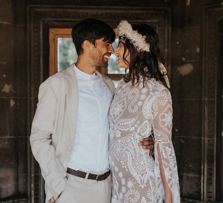 Groom in a beige suit embracing his bride in a lace wedding dress with long sleeves 