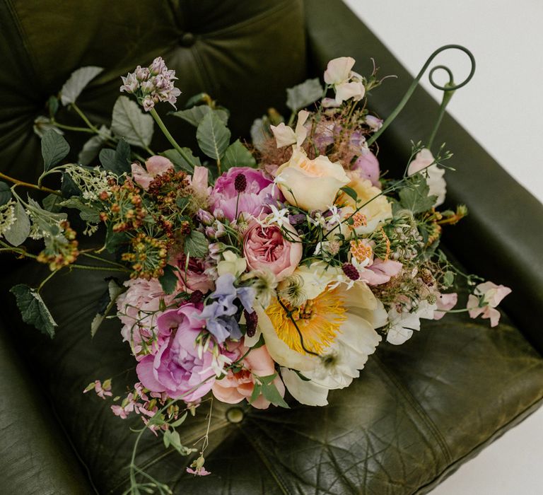 Multicoloured bridal bouquet with roses and green foliage on green leather chair for wedding at Loft Studios London 